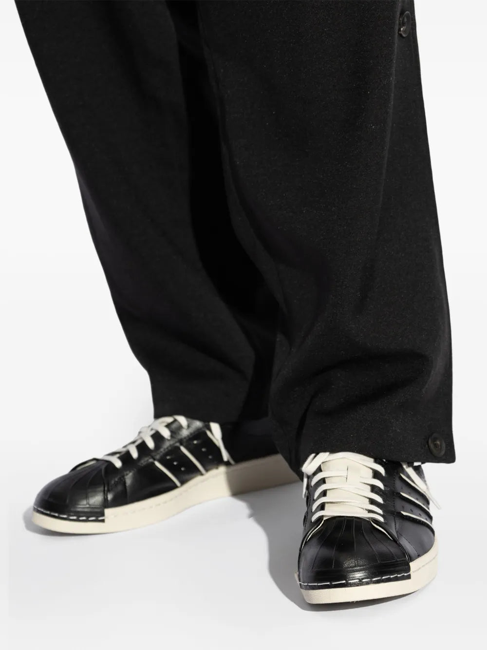 Black sneakers with white laces worn with black trousers, side angle