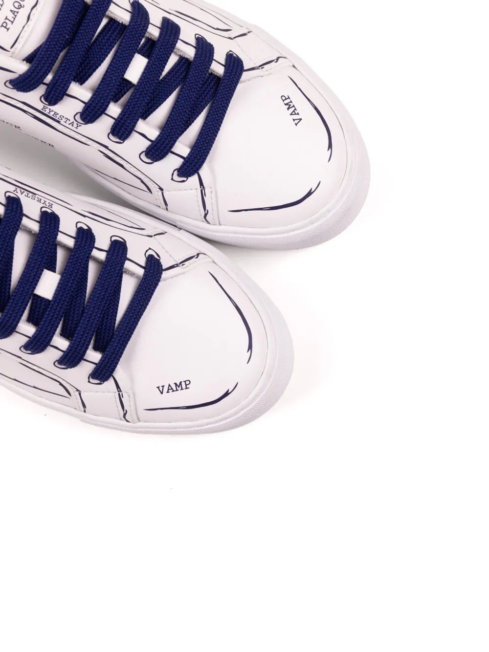 Close-up of white sneakers with navy-blue laces and 'VAMP' logo patch