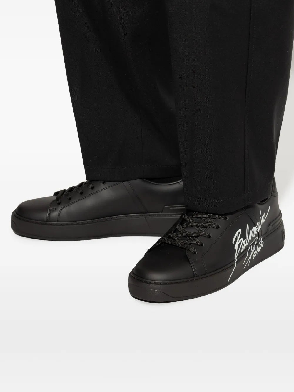 Black leather low-top sneakers worn with black trousers, side logo visible
