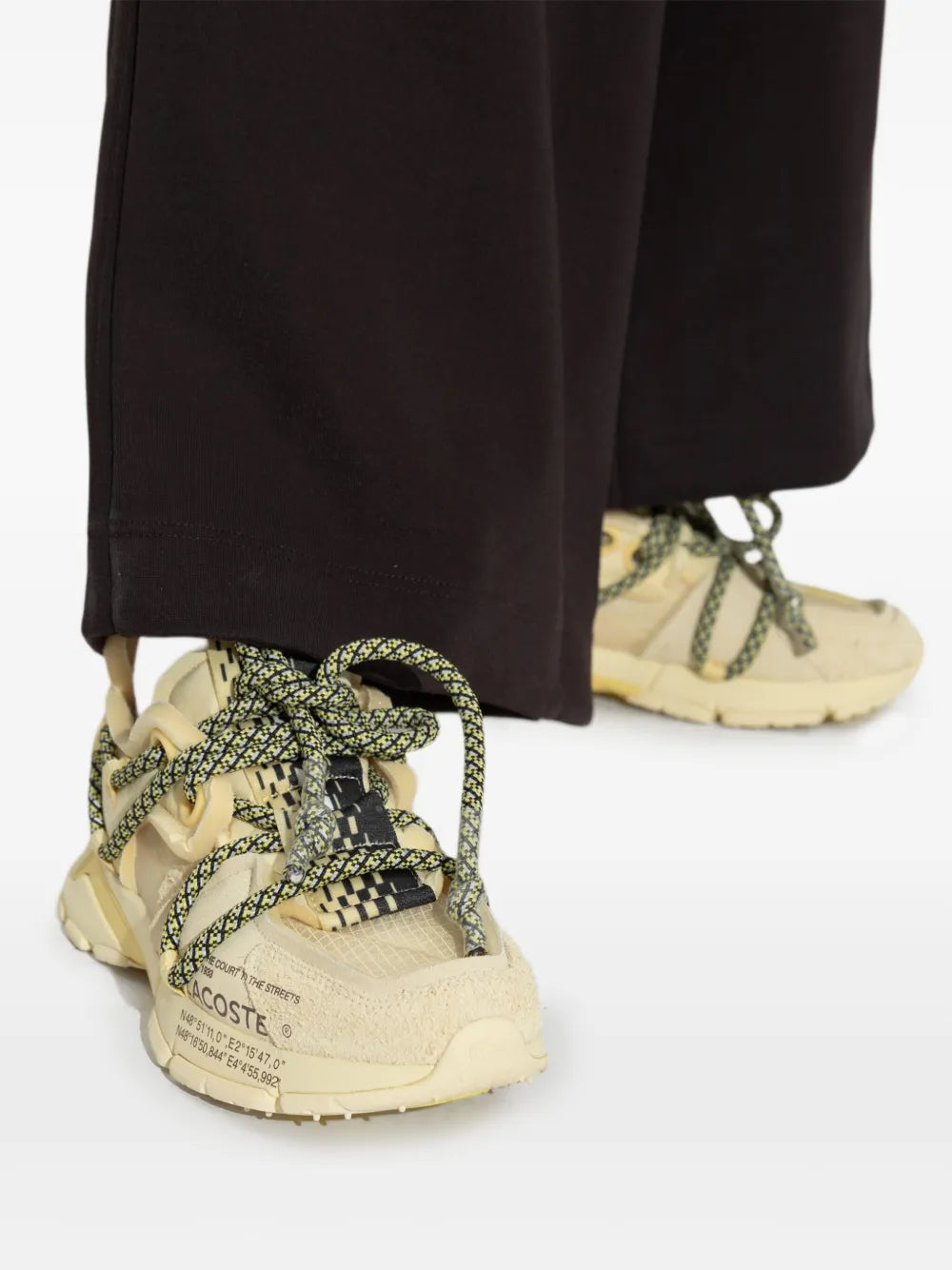 Close-up of yellow Lacoste mesh sneakers under black wide-leg pants