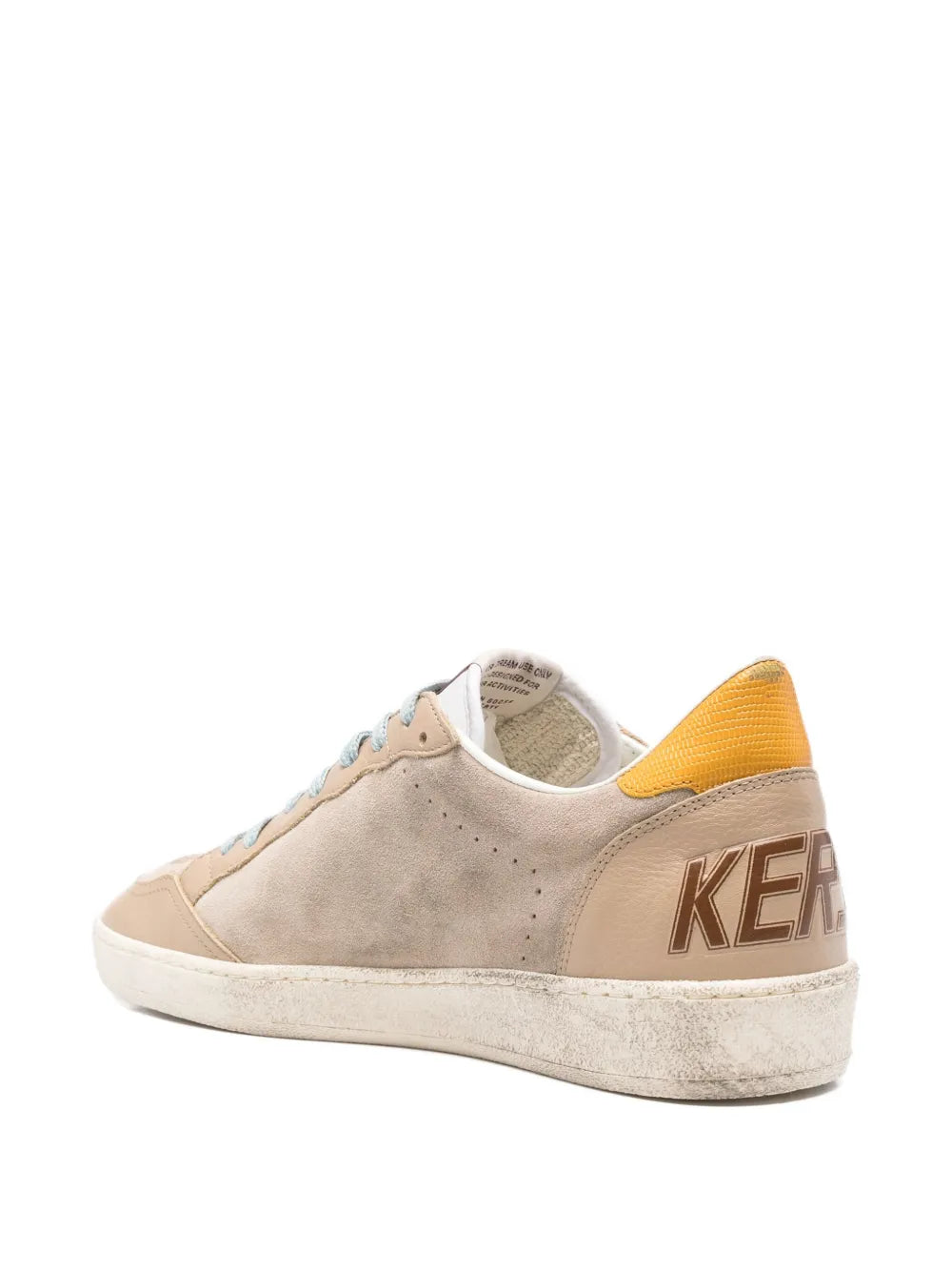 Beige low-top sneaker with yellow heel panel and side text detail on the quarter