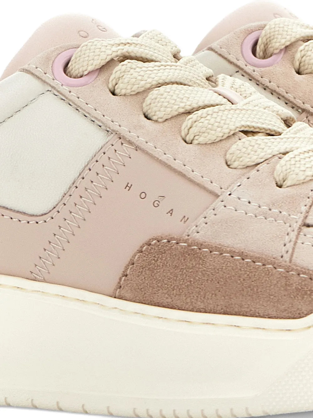 Close-up of pink and tan sneaker upper with stitching, lace eyelets, and logo detail
