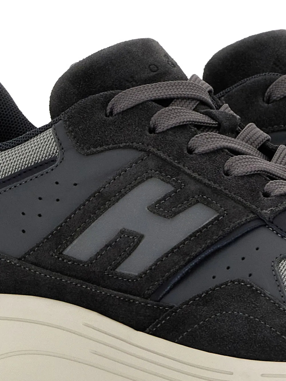 Close-up of black suede-look sneaker upper with gray H logo and lace eyelets