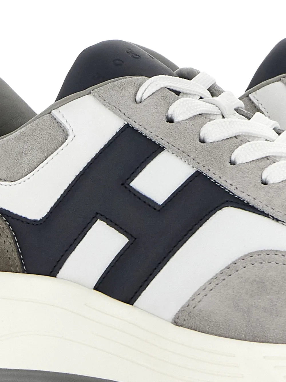 Close-up of white and gray lace-up sneakers with navy H-style stripe detail