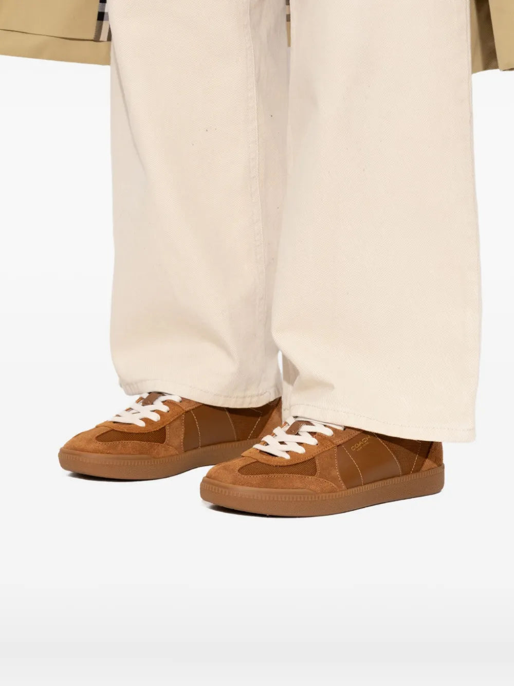 Brown COACH sneakers with white laces paired with off-white pants