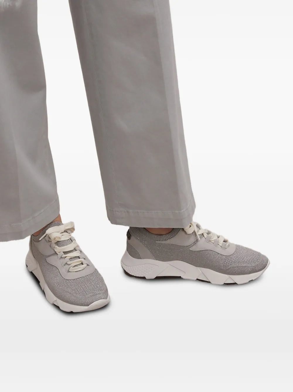 Grey knit lace-up sneakers on feet with white soles; worn with light trousers