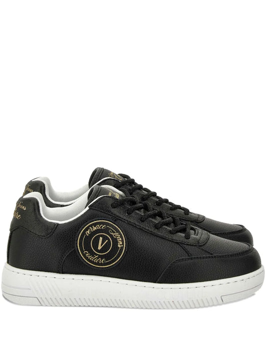 Black lace-up sneakers with round gold logo patch and white rubber sole