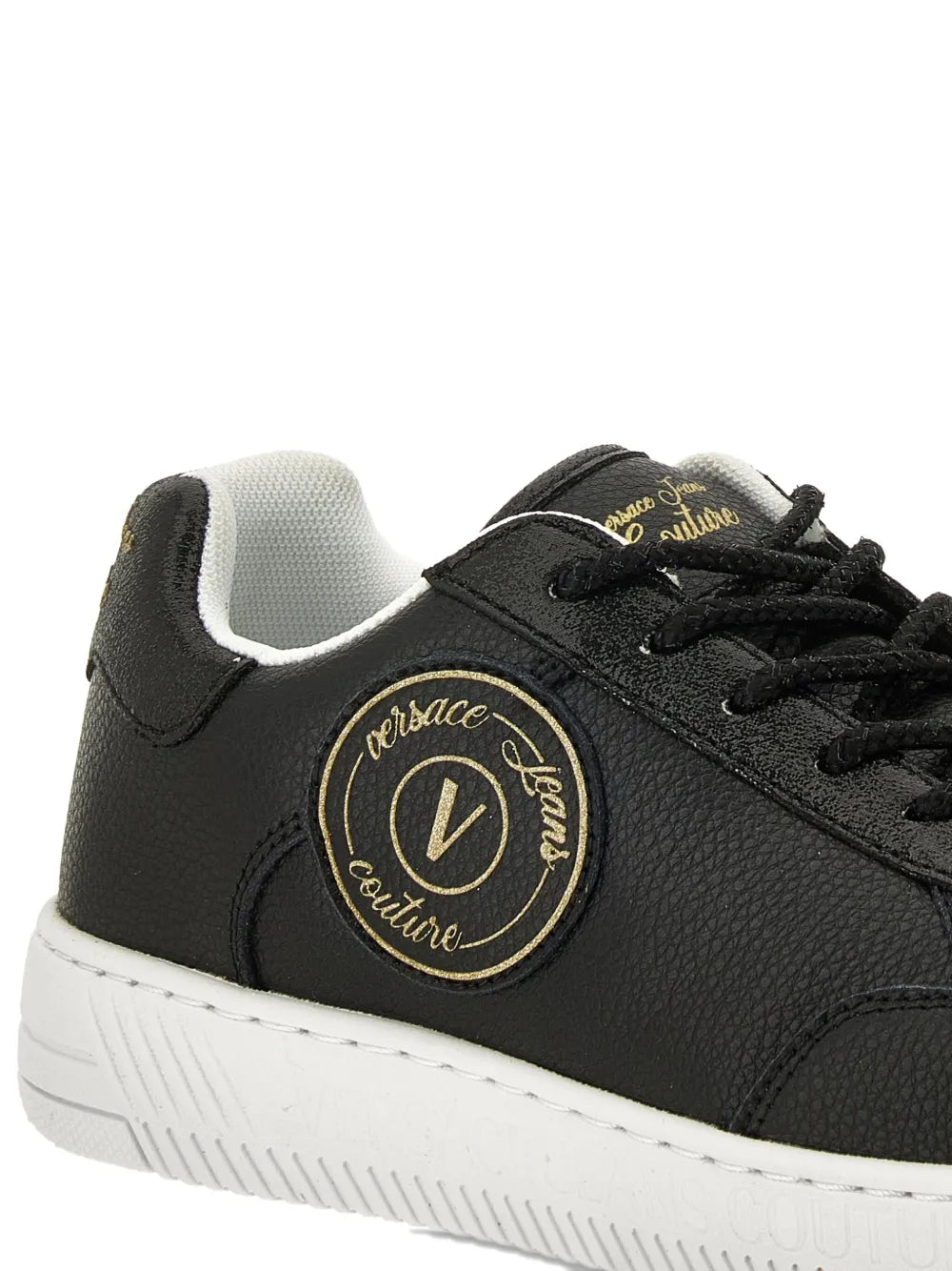Close-up of black sneakers with round gold logo patch, laces, and white sole
