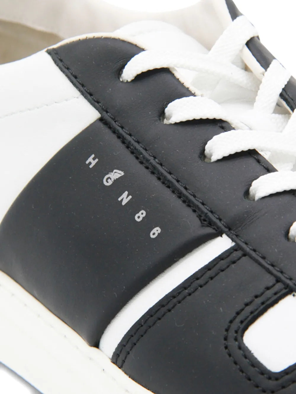 Black leather sneaker side panel with stitched detailing, white laces, and logo
