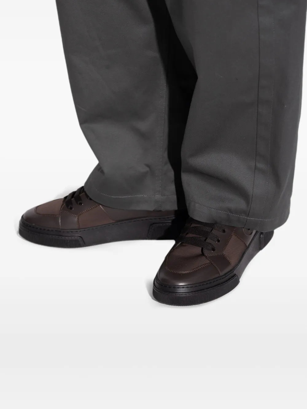 Brown leather sneakers with black laces, worn with dark trouser cuffs