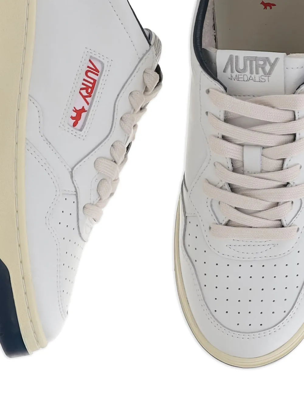Close-up of white leather low-top sneakers with red side logo and perforated toe