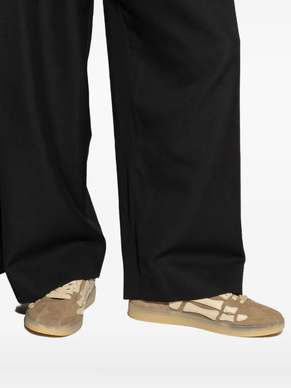 Light brown sneakers with bone print detailing, worn with black pants hem