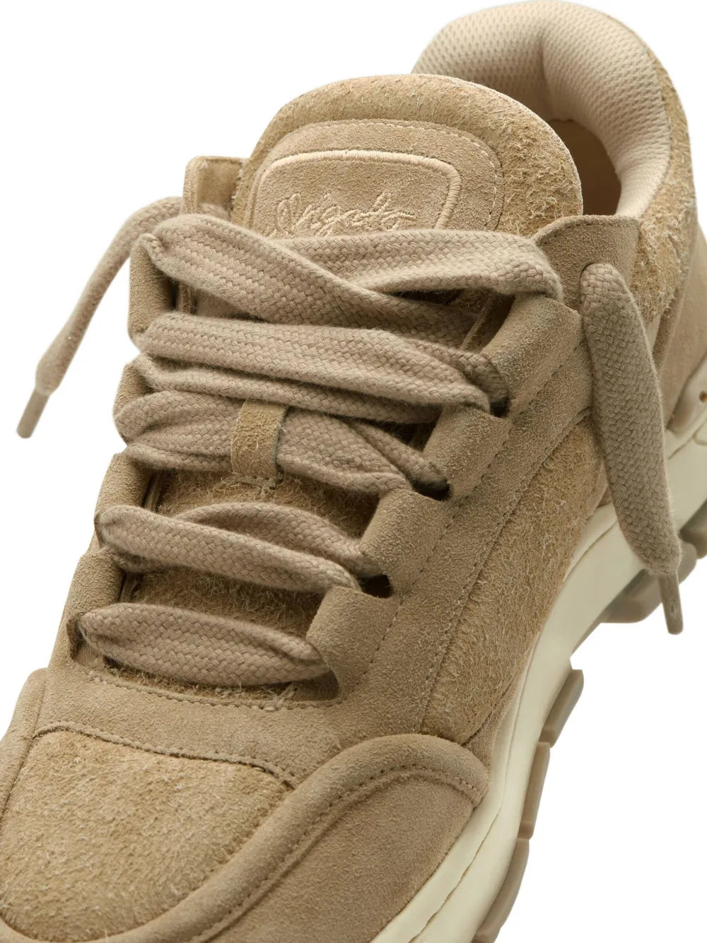 Light brown suede sneaker close-up, textured upper with lace loops and stitching.