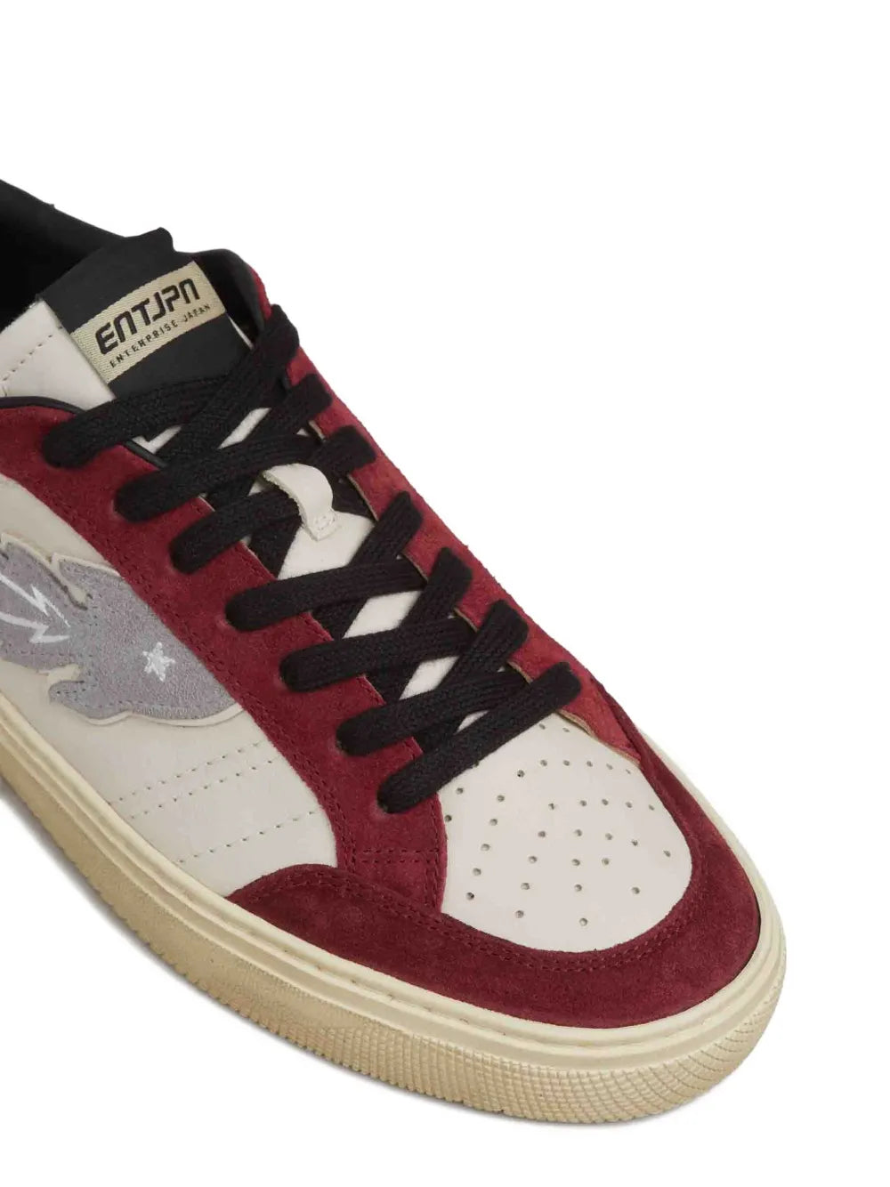 Close-up lace-up sneakers with red suede uppers, white panels, and black laces