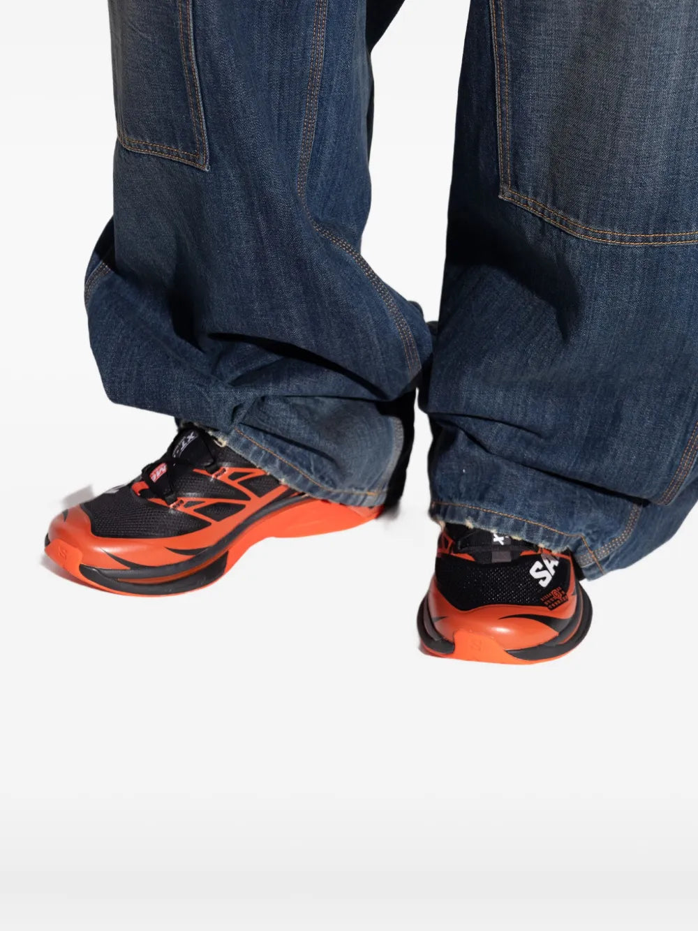 Orange and black lace-up sneakers worn with dark blue jeans cuffs.