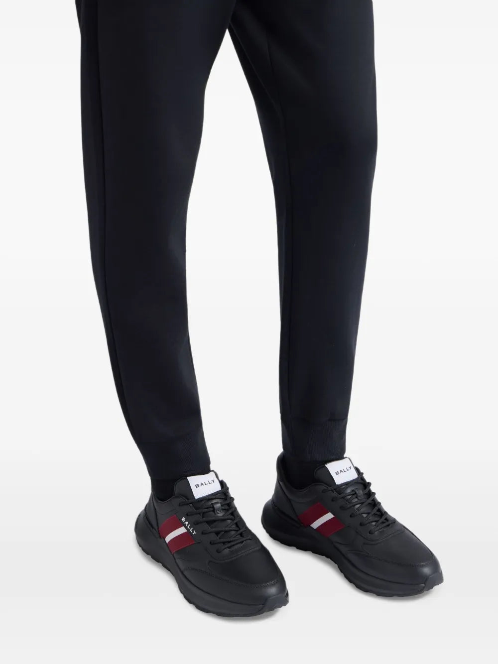Black leather sneakers with red and white stripe worn with dark pants