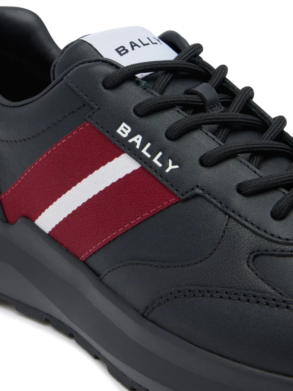 Black leather sneaker detail with red panel and white stripe near laces