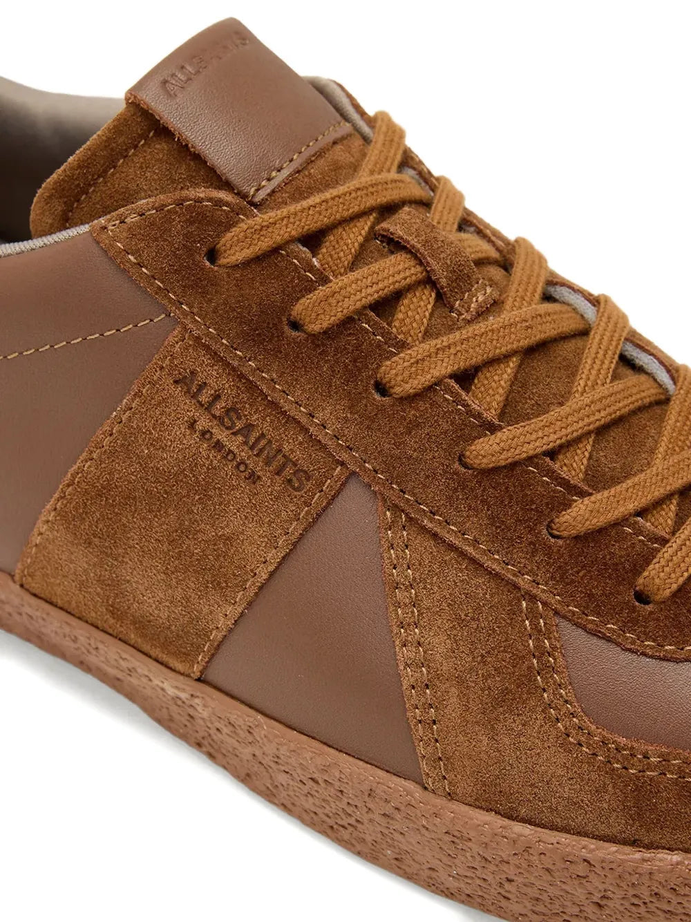 Close-up of brown lace-up sneakers with stitched seams, suede overlays, and Allsaints logo