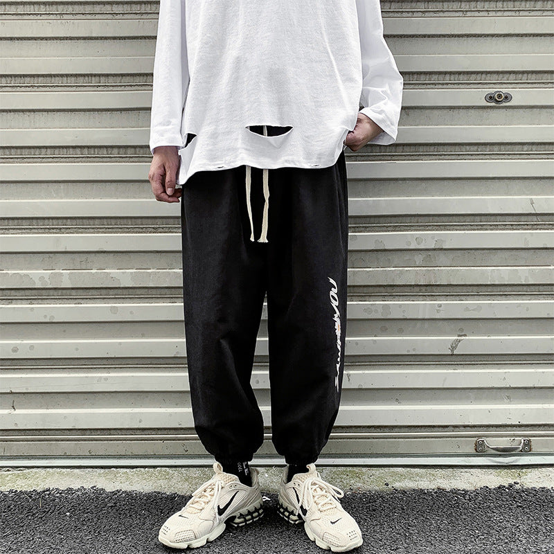 Black jogger trousers with drawstring waist, tapered legs, elastic ankle cuffs, side script