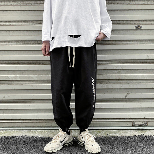 Black jogger trousers with drawstring waist, tapered legs, elastic ankle cuffs, side script