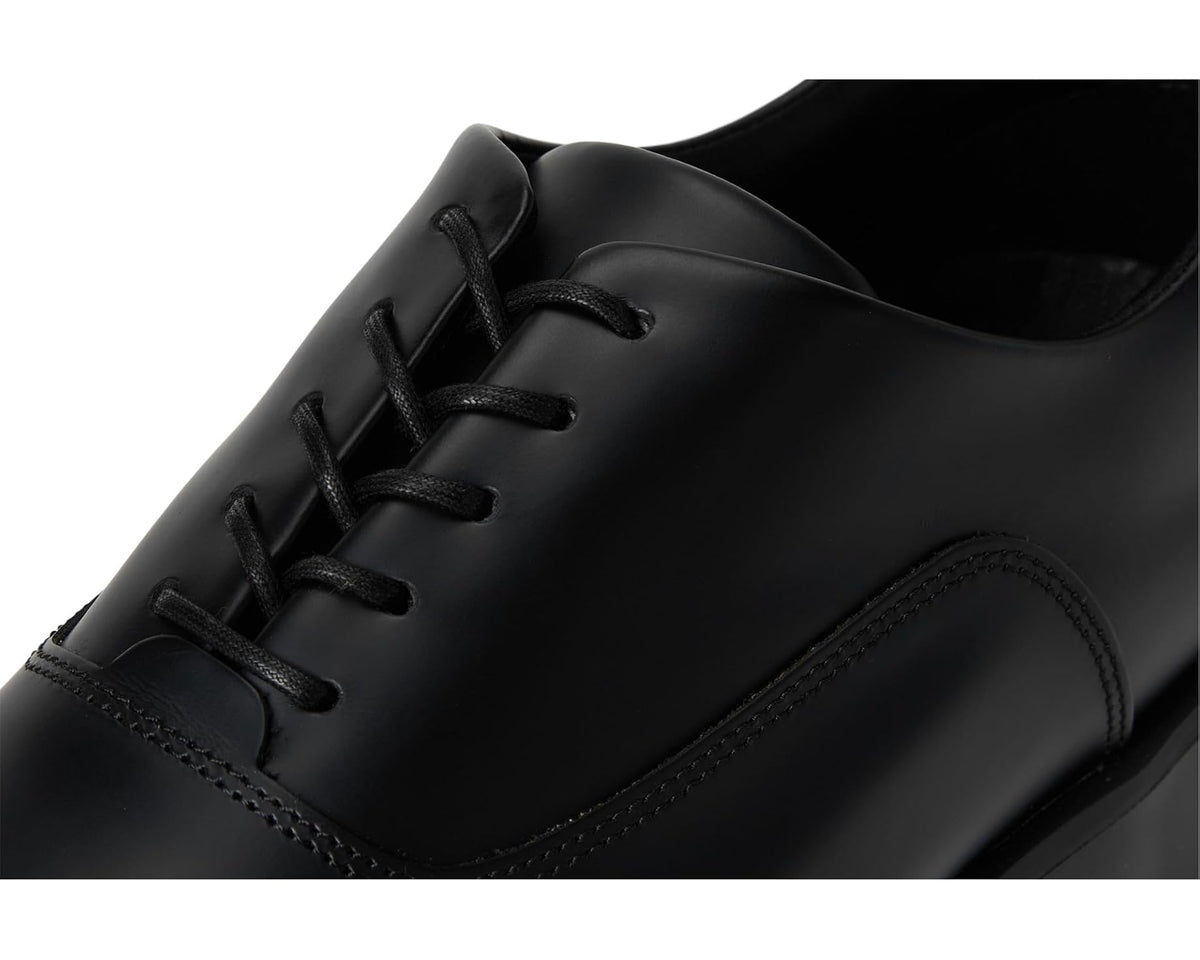Black leather oxford shoe close-up with lace eyelets and stitched toe seam