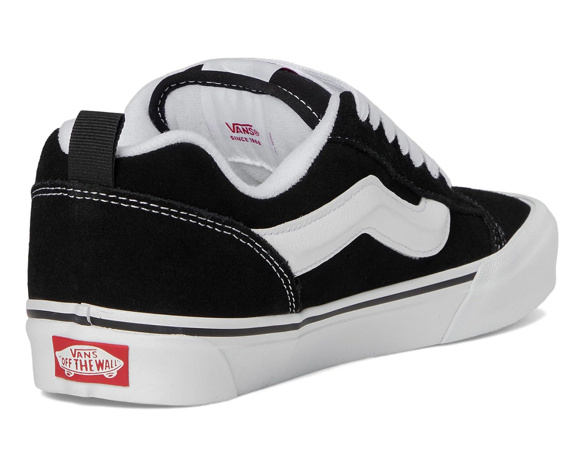 Black low-top sneakers with rear strap, Vans heel patch, and white midsole