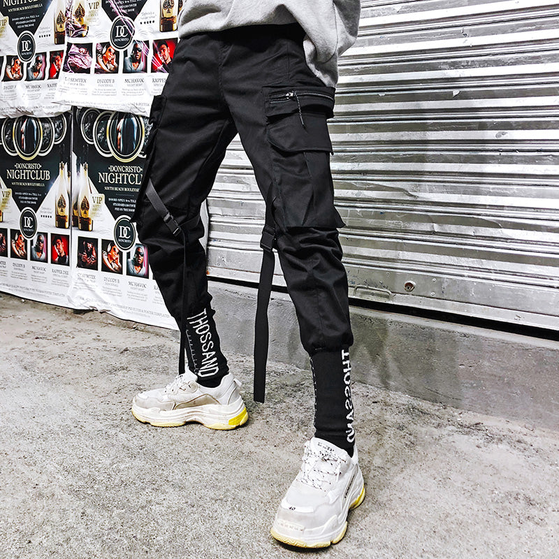 Black cargo pants with side flap pocket, straight leg, and belt tie straps at hem
