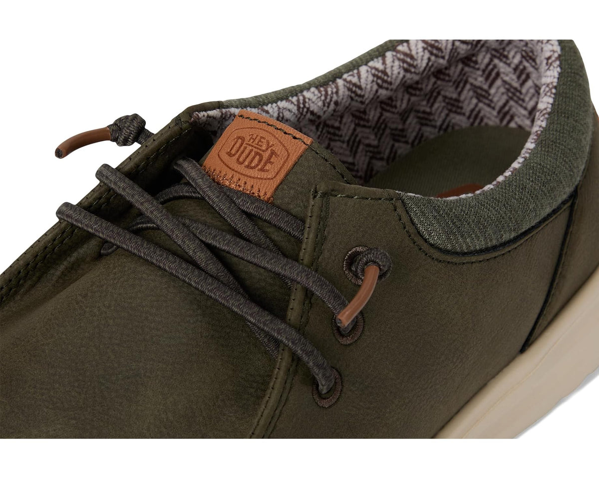 Olive lace-up casual shoe close-up with brown leather patch and metal eyelets