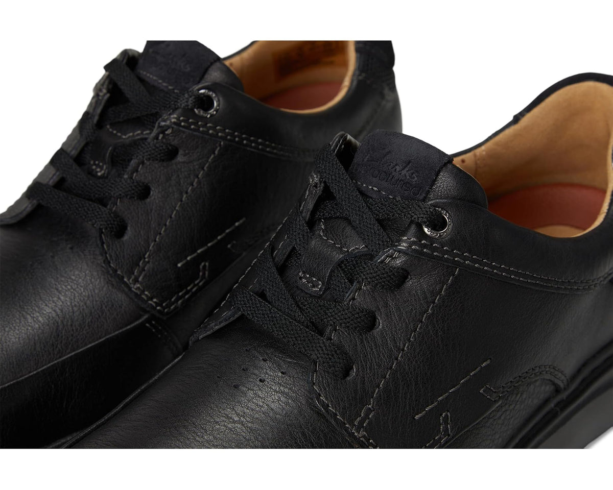 Close-up of black leather lace-up with eyelets, stitching, and padded tongue.