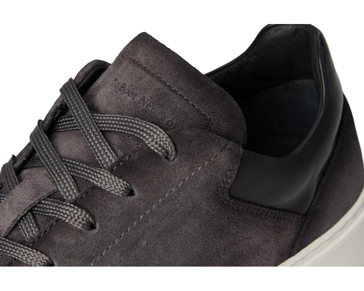 Men's grey suede sneakers close-up of laces, stitched eyelets, and logo patch